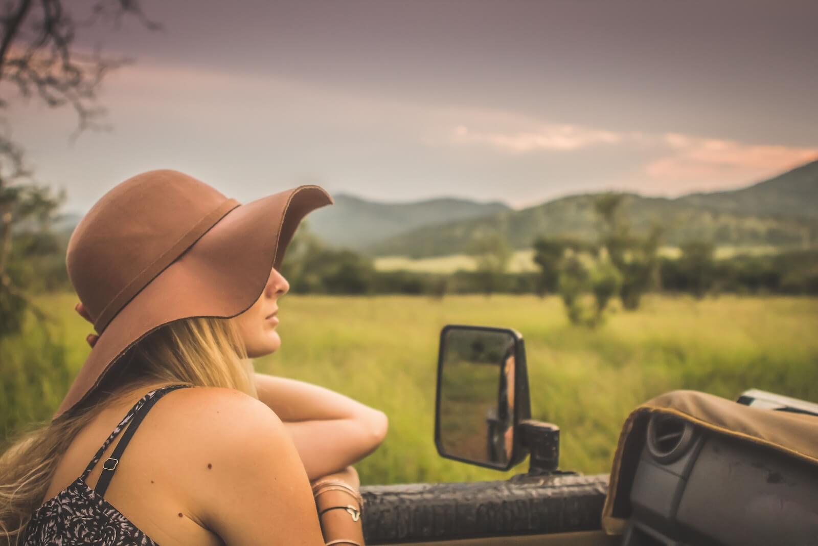 A woman in a large sun hat leans from a safari vehicle, gazing peacefully at the uncrowded Zululand landscape at sunset.