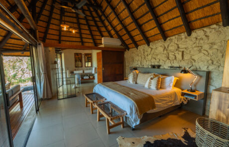 Interior of a thatched honeymoon suite with stone walls and private deck at Leopard Mountain